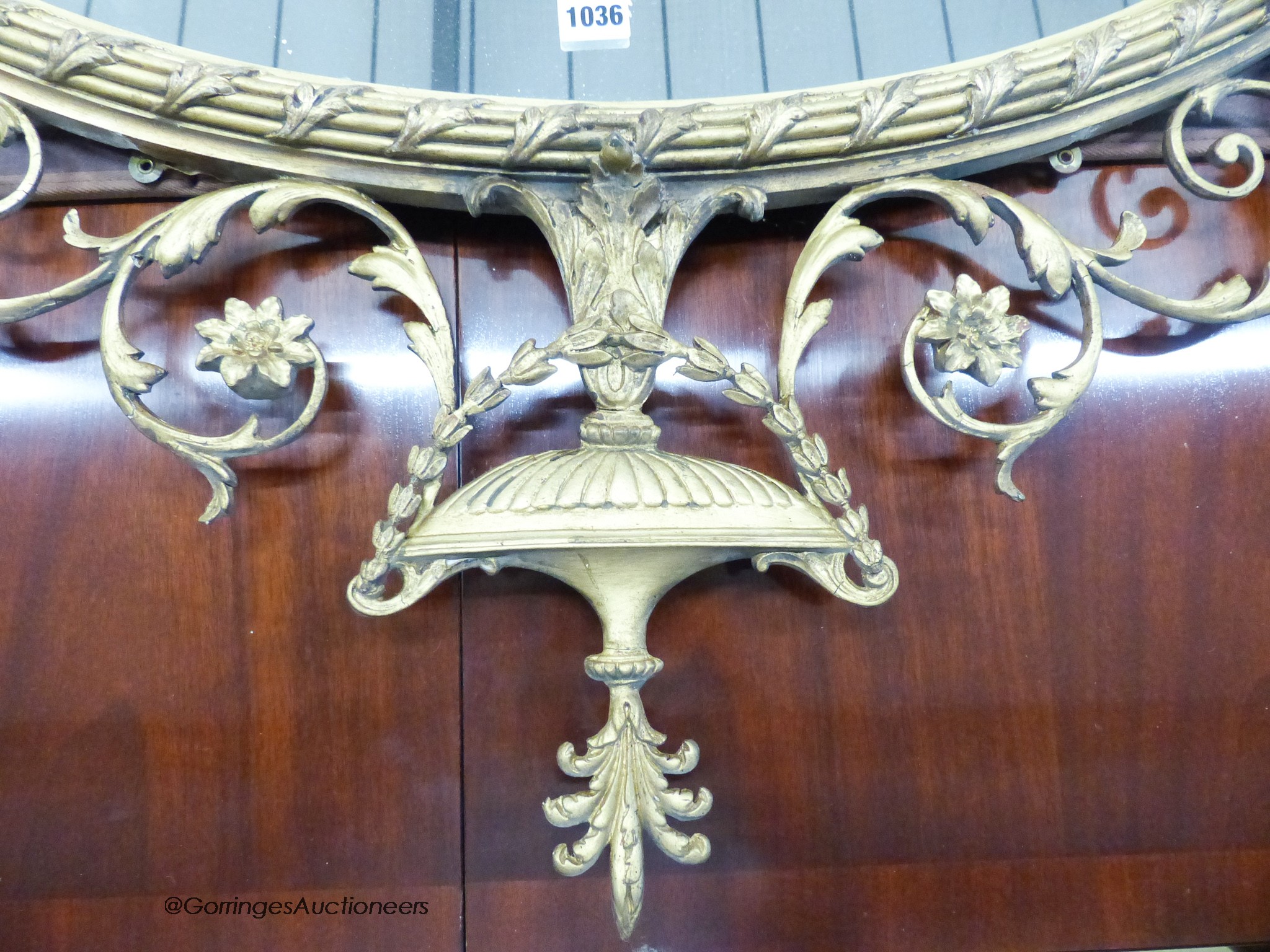 A 19th century regency style oval gilt wood and gesso wall mirror with urn finial. W-113, H-116cm.